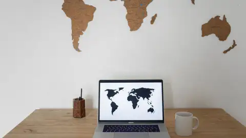 Ein Laptop mit einer Weltkarte auf dem Bildschirm, darüber eine Wandkarte